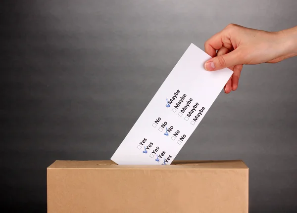 Mano con scheda elettorale e scatola su sfondo grigio — Foto Stock