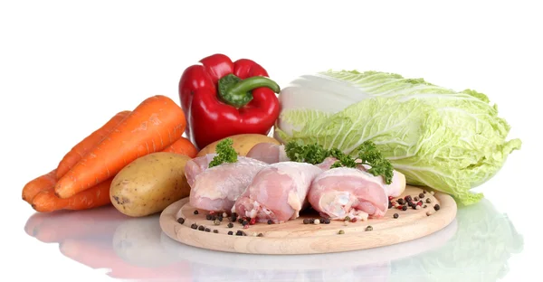 Légumes frais avec pilons de poulet crus et steak de porc sur planche à découper isolé sur blanc — Photo