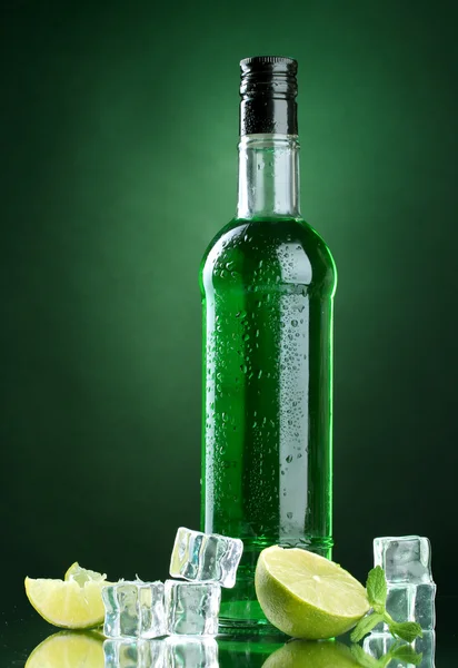 Bottle of absinthe with lime and ice on green background — Stock Photo, Image