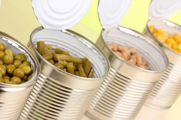 Boîtes de conserve ouvertes de pois, maïs, haricots et haricots français sur table en bois sur fond vert — Photo