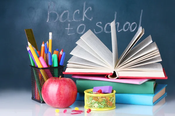 Samenstelling van boeken, briefpapier en een appel op de leraar Bureau in de achtergrond van het bord. terug naar school. — Stockfoto