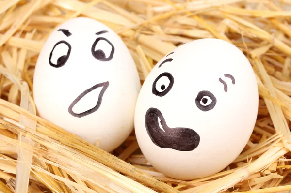Белые яйца со смешными лицами в соломе — стоковое фото