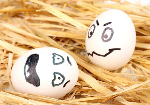 Huevos blancos con caras graciosas en paja —  Fotos de Stock