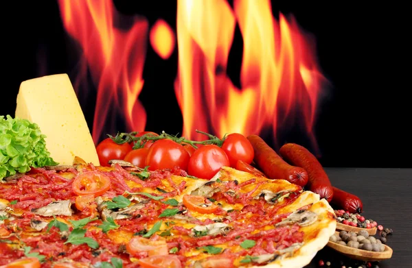 Güzel pizza, salam, domates ve baharatlar alev arka plan üzerinde ahşap tablo — Stok fotoğraf