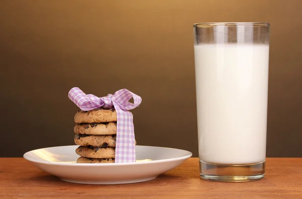 Vaso de leche y galletas sobre mesa de madera sobre fondo marrón — Foto de Stock