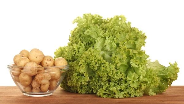 stock image Young potatoes in a glass bowl with lettuce on a table on white background