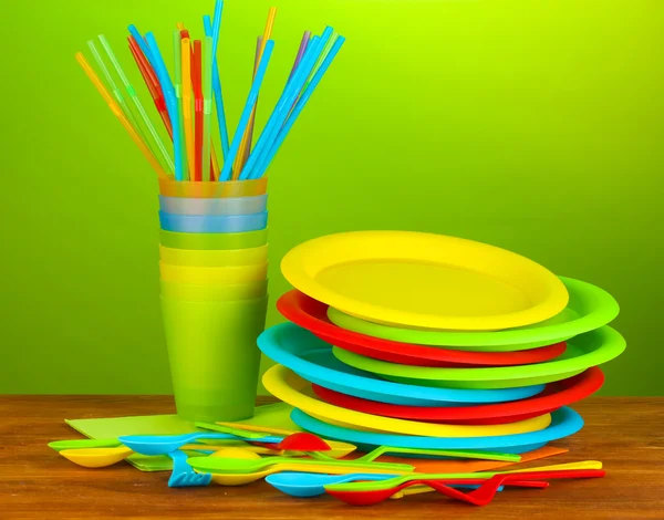 Bright plastic disposable tableware on wooden table on colorful background — Stock Photo, Image