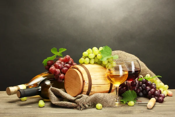Vat, flessen en glazen wijn en rijpe druiven op houten tafel op grijze achtergrond — Stockfoto