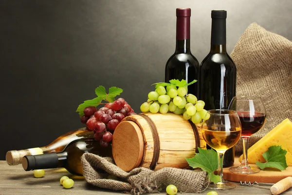 Fass, Flaschen und Gläser mit Wein, Käse und reifen Trauben auf Holztisch vor grauem Hintergrund — Stockfoto