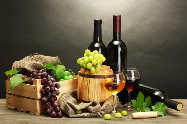 Barel, lahve a sklenice vína a zralé hrozny na dřevěný stůl na šedém pozadí — Stock fotografie