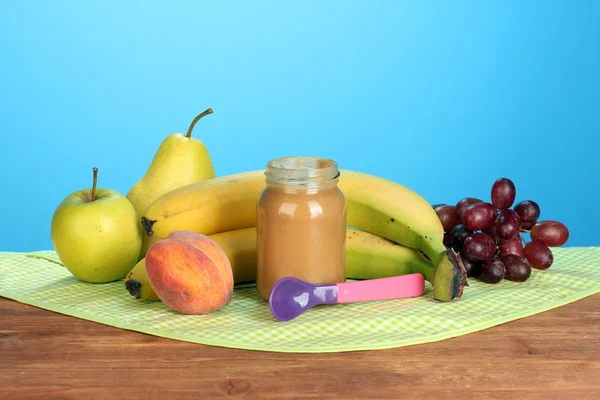 Glas mit Obst Babynahrung, Löffel und Früchten auf bunter Serviette auf blauem Hintergrund — Stockfoto