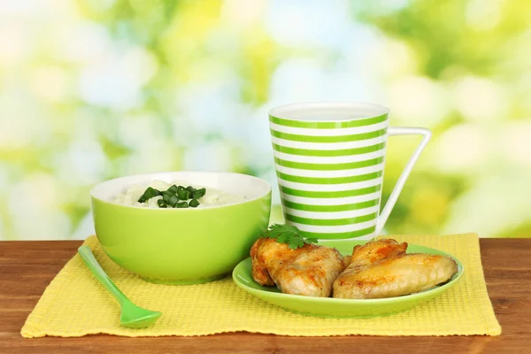 Mashed potato in the bowl and roasted chicken wings in the plate and cup with milk on colorful napkin on wooden table close-up — Stock Photo, Image