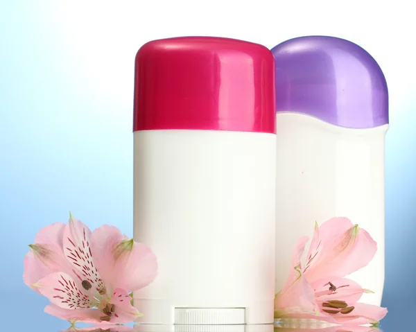 Deodorants with flowers on blue background — Stock Photo, Image