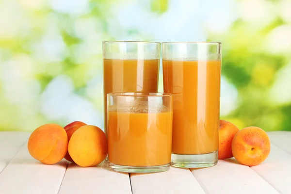 Gläser Marillensaft und frische Aprikosen auf weißem Holztisch auf grünem Hintergrund — Stockfoto