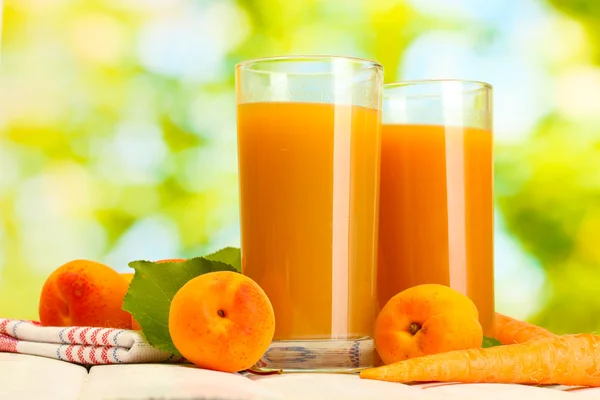 Glasögon med morot och aprikos juice på vita träbord på grön bakgrund — Stockfoto
