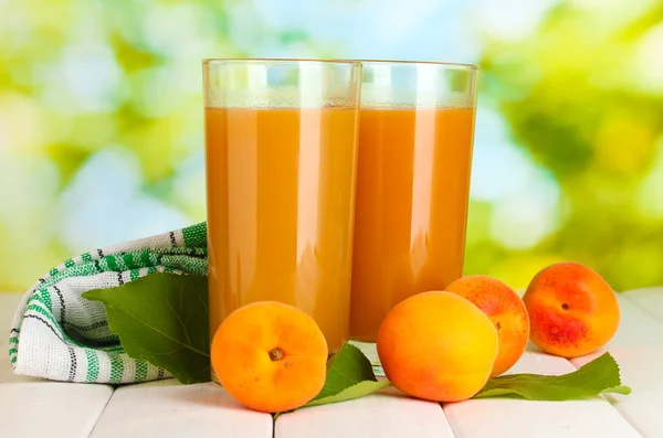 Glasögon av aprikos juice och färska aprikoser på vita träbord på grön bakgrund — Stockfoto