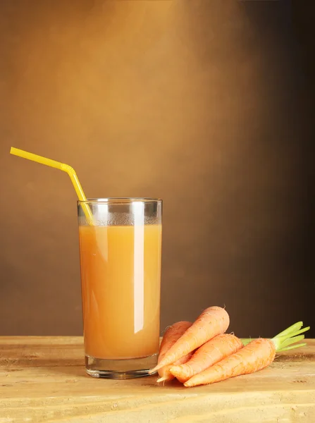 Vaso de jugo de zanahoria sobre mesa de madera sobre fondo marrón —  Fotos de Stock
