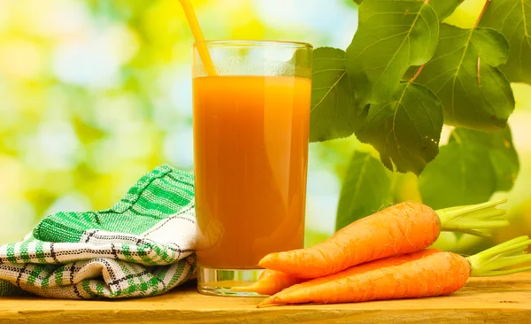 Glass of carrot juice and fresh carrots on wooden table on green background — Stock Photo, Image