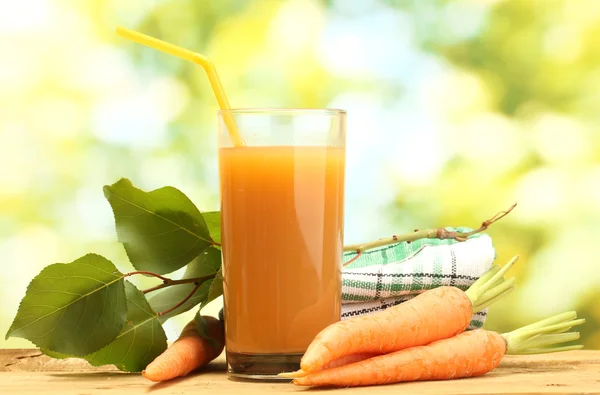Ποτήρι χυμό καρότου και φρέσκα καρότα σε ξύλινο τραπέζι σε πράσινο φόντο — Φωτογραφία Αρχείου