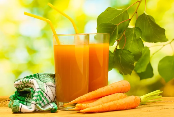 Verres de jus de carotte et de carottes fraîches sur table en bois sur fond vert — Photo