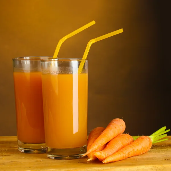 Glasses of carrot juice on wooden table on brown background — Stock Photo, Image