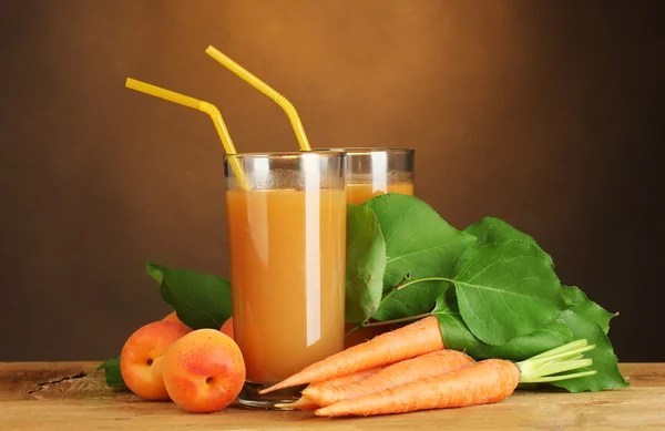 Bicchieri di succo di carota e albicocca su tavolo di legno su sfondo marrone — Foto Stock