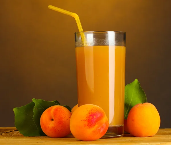 Glass of apricot juice on wooden table on brown background — Stock Photo, Image