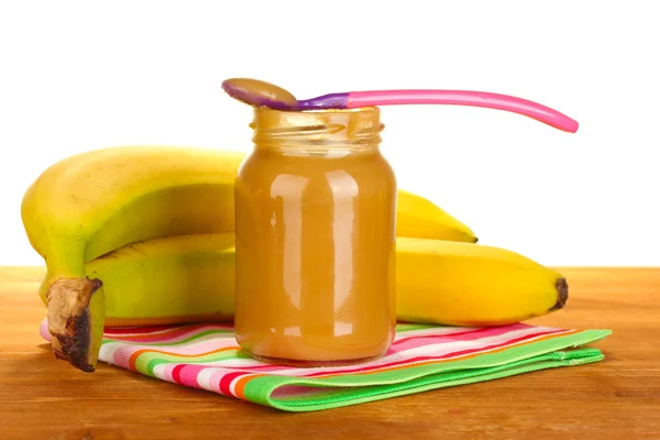 Burk med banana barnmat, sked och bananer på färgglada servett på vit bakgrund närbild Stockbild
