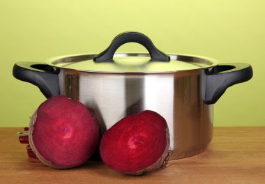 Young red beet and pan on wooden table on green background clipart