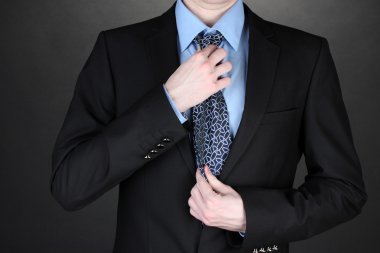 Businessman correcting a tie on black background clipart