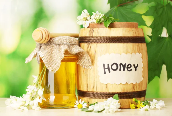 Dolce miele in botte e vaso con fiori di acacia su tavola di legno su fondo verde — Foto Stock