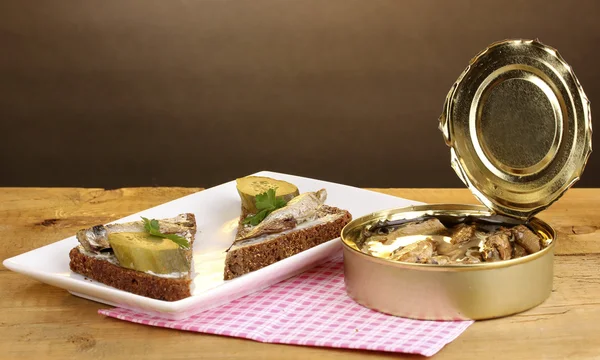 stock image Tasty sandwiches with sprats on plate on wooden table on brown background