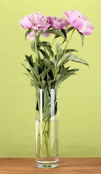 Trois pivoines roses dans un vase sur une table en bois sur fond vert — Photo