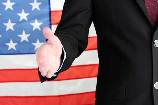 アメリカの国旗の背景に握手を求めて彼の手を与えることの実業家 — ストック写真