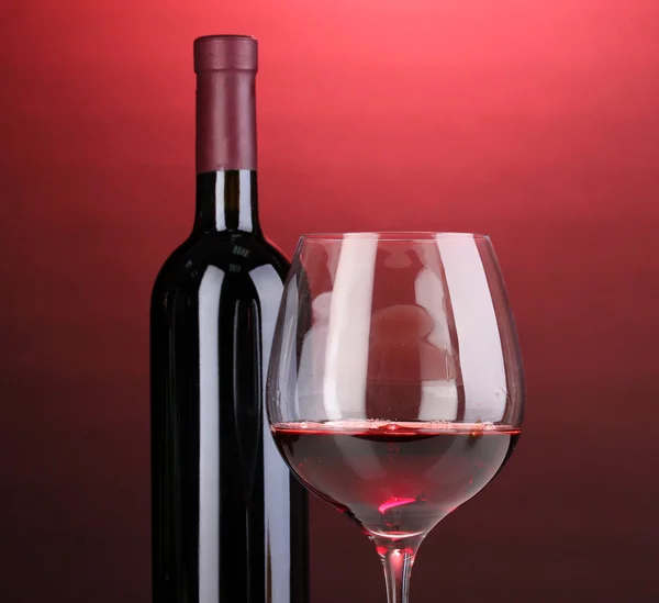 Láhev skvělé víno a skleničku na červeném pozadí — Stock fotografie