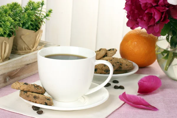 Taza de café, galletas, naranja y flores en la mesa en la cafetería — Foto de Stock