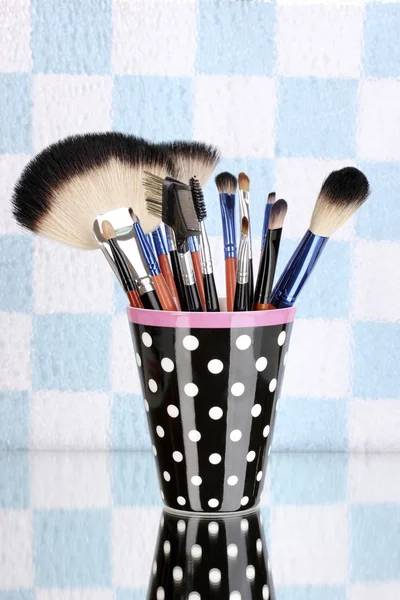Makeup brushes in a black polka-dot cup on colorful background — Stock Photo, Image