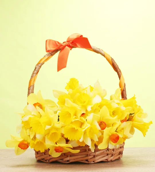 Beautiful yellow daffodils in basket with bow on wooden table on green background — Stock Photo, Image