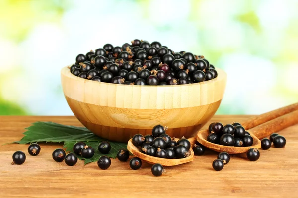 Fresh black currant in wooden bowl on green background close-up — Stock Photo, Image
