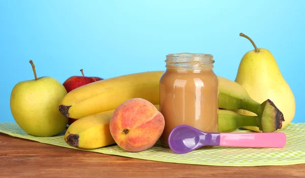 Frasco com alimentos para bebês de frutas, colher e frutas em guardanapo colorido no fundo azul — Fotografia de Stock