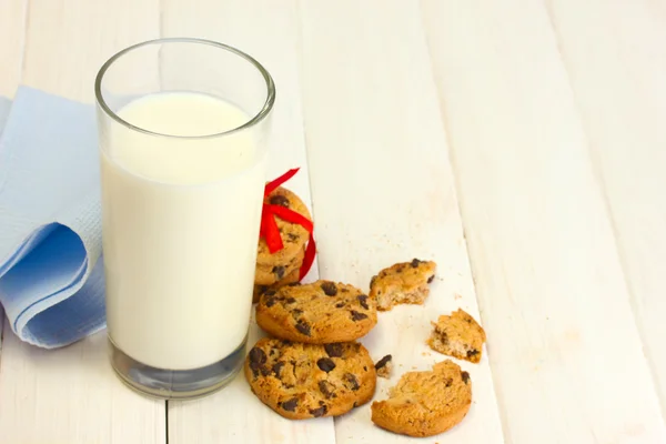 Glass of milk and chocolate chips cookies with red ribbon on wooden table — Stock Photo, Image