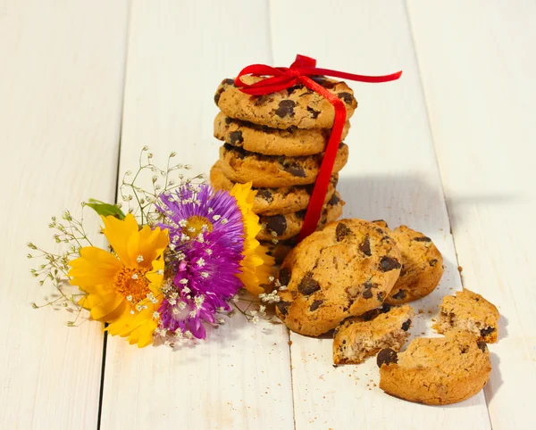 Biscuits aux pépites de chocolat avec ruban rouge et fleurs sauvages sur table en bois — Photo