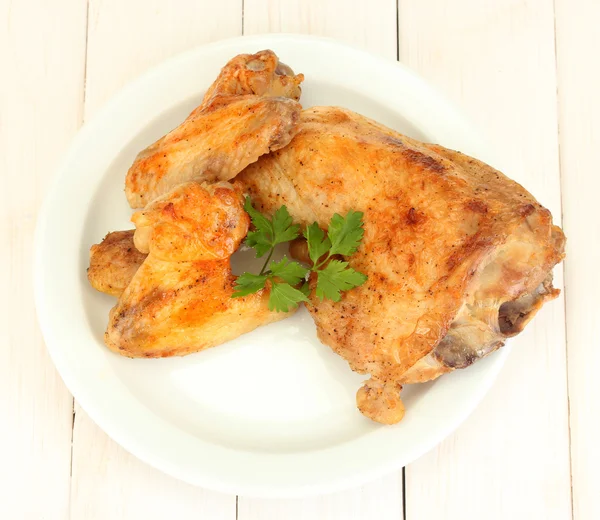 Alitas de pollo tostadas y pierna con perejil en el plato sobre fondo de madera blanca de cerca — Foto de Stock