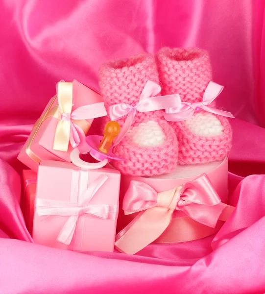 Rózsaszín bébi csizma, cumi, ajándékok, selyem háttér — Stock Fotó