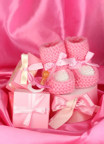 Розовые сапоги, соска, подарки на шелковом фоне — стоковое фото