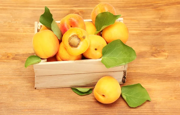 Спелые абрикосы с зелеными листьями в деревянной коробке на деревянном столе — стоковое фото