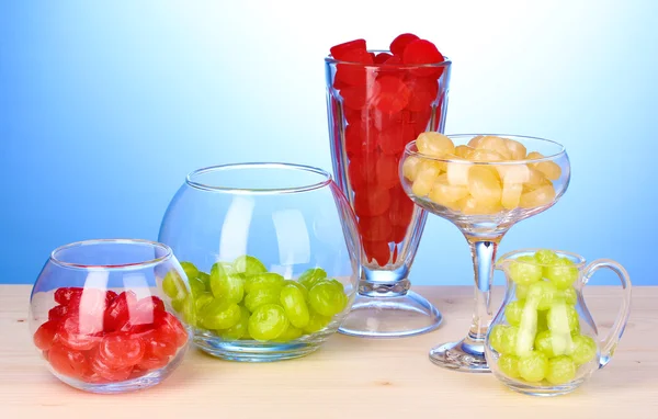 Color candies in glasses on wooden table on blue background — Stock Photo, Image