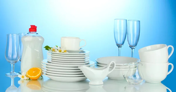 Tom ren tallrikar, glas och koppar med diskmedel och citron på blå bakgrund — Stockfoto