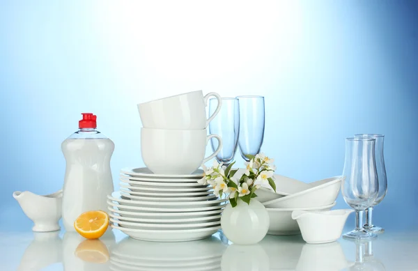 stock image Empty clean plates, glasses and cups with dishwashing liquid and lemon on blue background