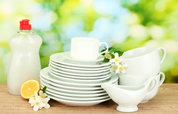Lege schoon borden en kopjes met afwasmiddel, bloemen en citroen op houten tafel op groene achtergrond — Stockfoto